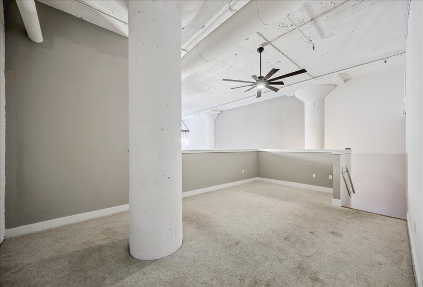 Spacious loft area featuring industrial-style concrete columns and exposed ductwork