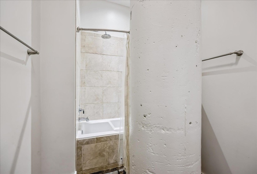 Tub/shower combination featuring a rainfall showerhead, beige tile surround, and clear glass shower screen