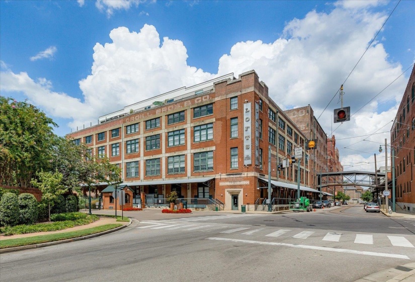Brick building featuring multiple stories, large windows, an overhead walkway, and street-level commercial spaces