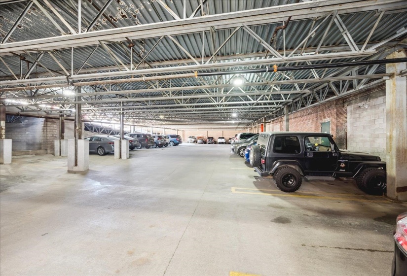 Expansive covered parking area featuring concrete flooring, exposed industrial ceiling trusses, and brick and block wall construction
