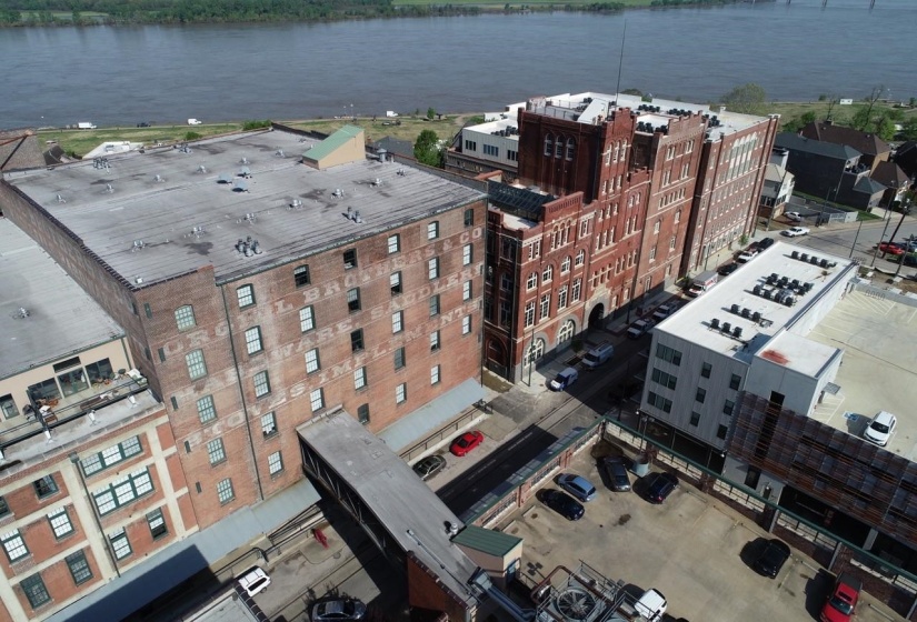 Historic brick building featuring multiple windows, a flat roof, and an overhead walkway connecting to an adjacent structure