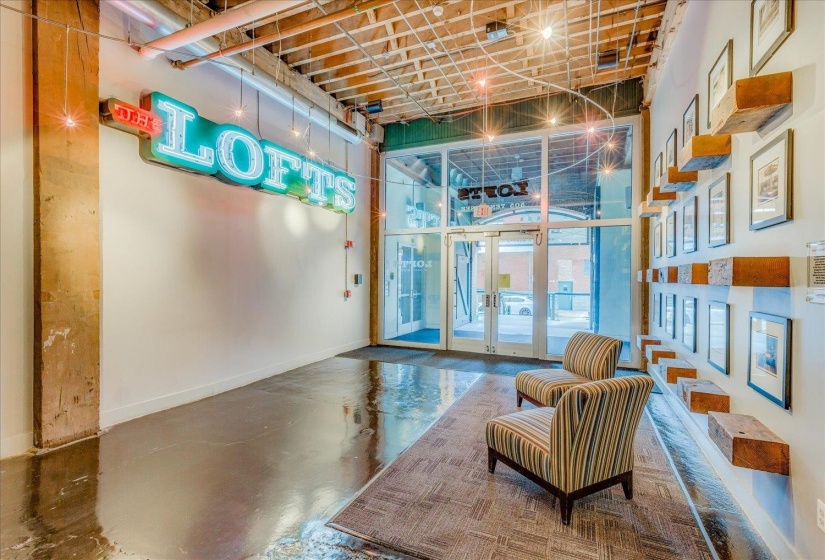 Entryway featuring a large glass storefront, exposed ceiling beams, polished concrete flooring, a decorative wall display, and a statement neon sign