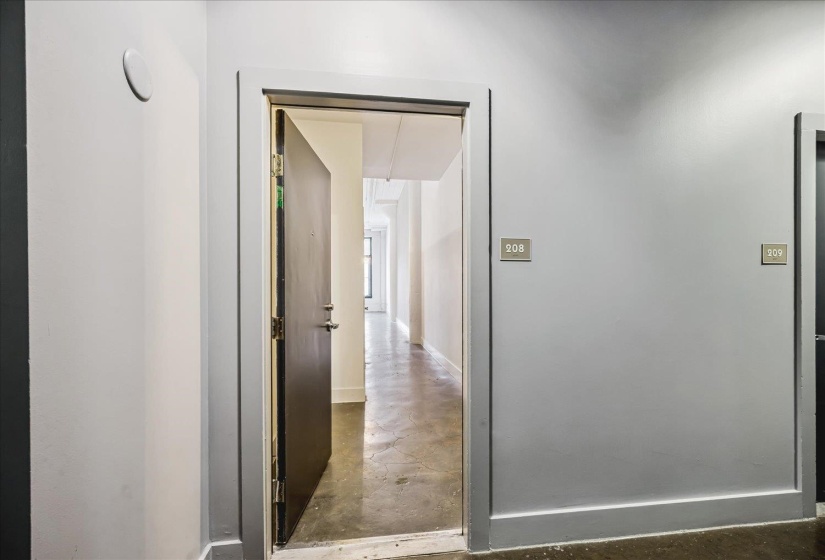 Entrance door with dark finish and visible hardware, concrete flooring, and light-toned walls