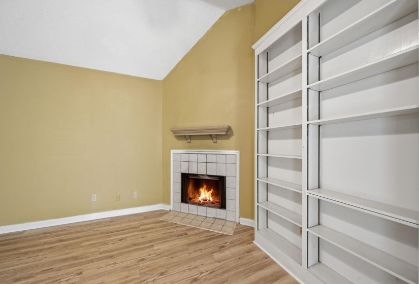 Vaulted ceiling room featuring a corner fireplace with a tiled surround, a decorative mantel, and wood-finish flooring