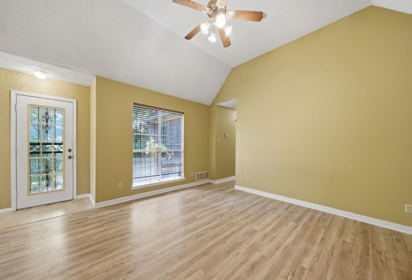 Spacious living area featuring vaulted ceilings, wood-finish flooring, and a decorative glass entry door