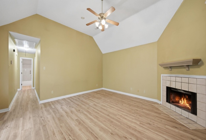 Spacious interior featuring vaulted ceilings, wood-finish flooring, a ceiling fan with light fixture, and a tiled corner fireplace with a wooden mantel