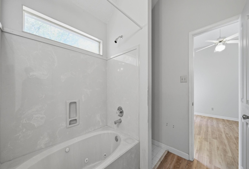 Bathroom featuring a jetted tub, shower with light-toned surrounds, and a transom window