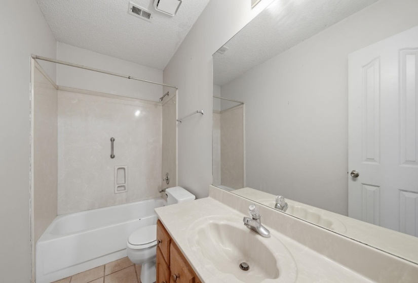 Full bathroom featuring a single vanity, integrated sink, large wall mirror, and a tub-shower combination with a textured surround