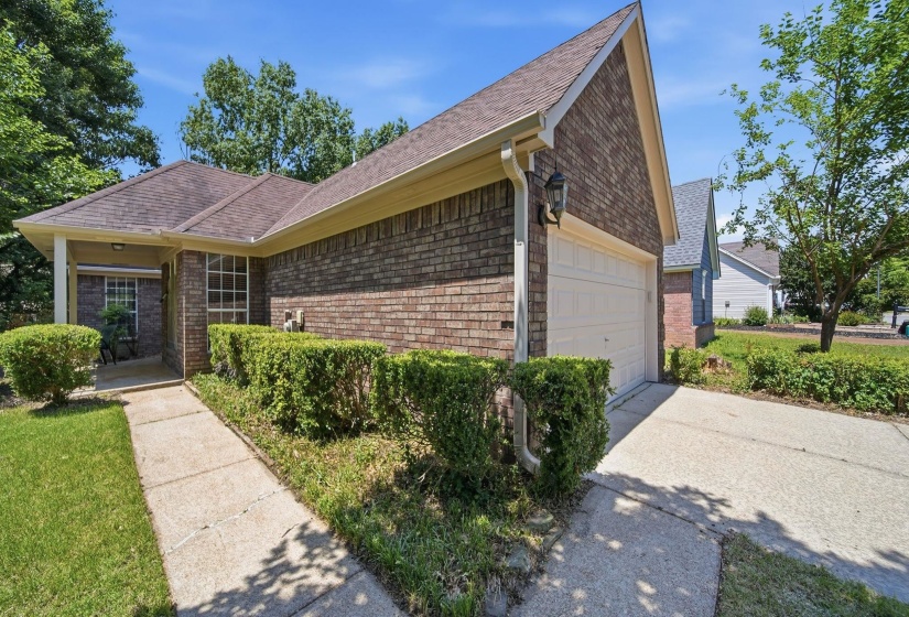 Brick exterior featuring a gabled roofline, an attached garage, a covered front entry, established landscaping, and a concrete driveway