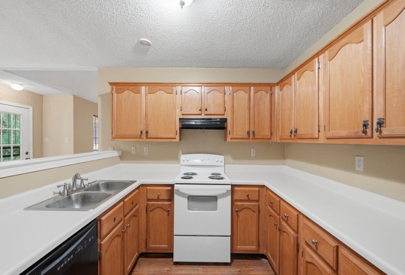 U-shaped kitchen featuring wood cabinetry, white countertops, a double basin stainless steel sink, and a white electric range with a black range hood