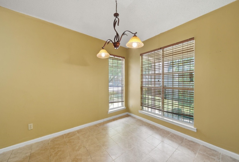 Room featuring tile flooring, two windows with blinds, a vaulted ceiling, and an ornate chandelier