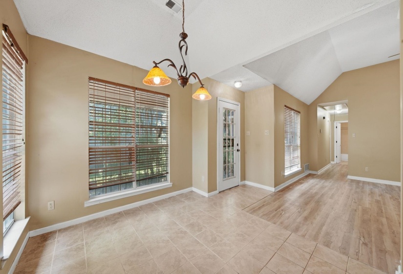 Spacious interior with vaulted ceilings, large windows featuring blinds, a glass-paneled door, and a mix of tile and wood-finish flooring