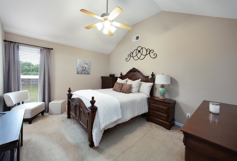 Spacious carpeted room featuring a vaulted ceiling with a ceiling fan, a large window with blinds and curtains, and neutral-toned wall paint