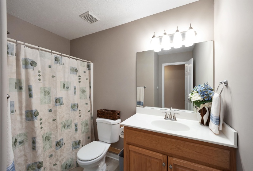 Bathroom featuring a light wood-finish vanity with a white countertop and integrated sink, a large wall-mounted mirror, and a four-bulb vanity light fixture
