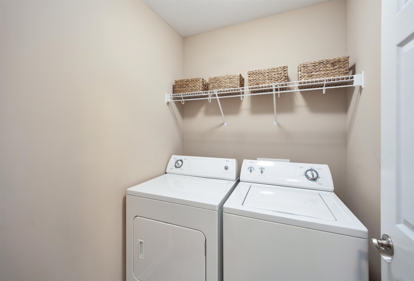 Dedicated laundry area featuring a white top-load washing machine, a white front-load dryer, and an overhead wire shelving unit