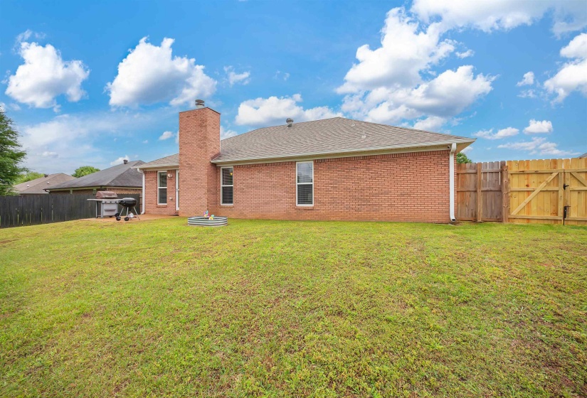 Expansive green lawn with a brick exterior, a prominent brick chimney, a brown shingled roof, and a wood privacy fence