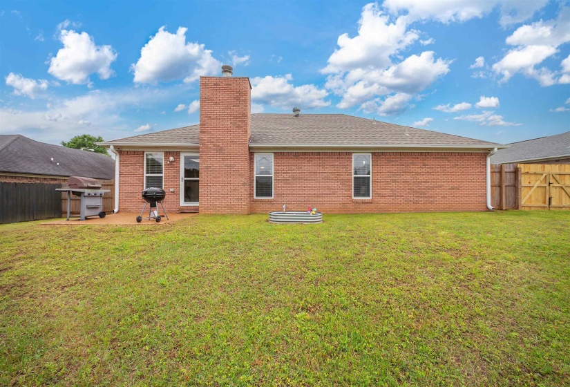 Expansive rear lawn featuring a brick exterior, a prominent brick chimney, a concrete patio area, and a privacy fence