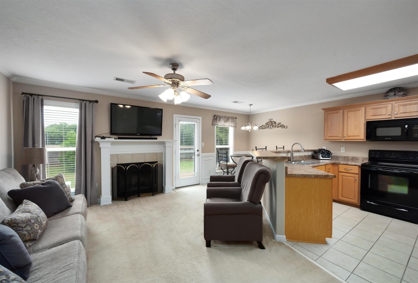Open-concept living space featuring a white fireplace mantel, ceiling fan, and carpeted flooring