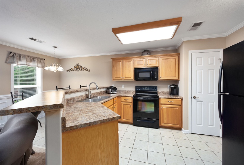 Kitchen featuring wood cabinetry, laminate countertops, stainless steel sink, black appliances, and tile flooring