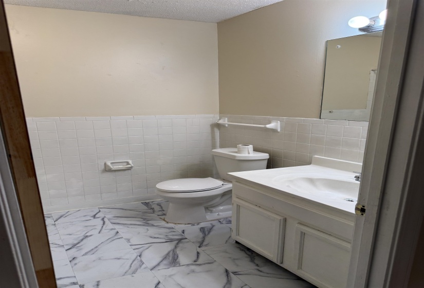 Bathroom with marble-look flooring, white tile wainscoting, and a white vanity with integrated sink