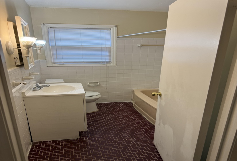 Bathroom featuring a built-in tub, white tile wainscoting, and a window with blinds