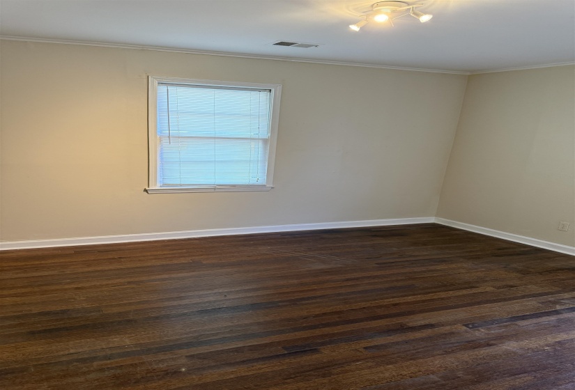Wood-finish flooring throughout, featuring a single window with blinds, white trim, and a ceiling-mounted track light fixture