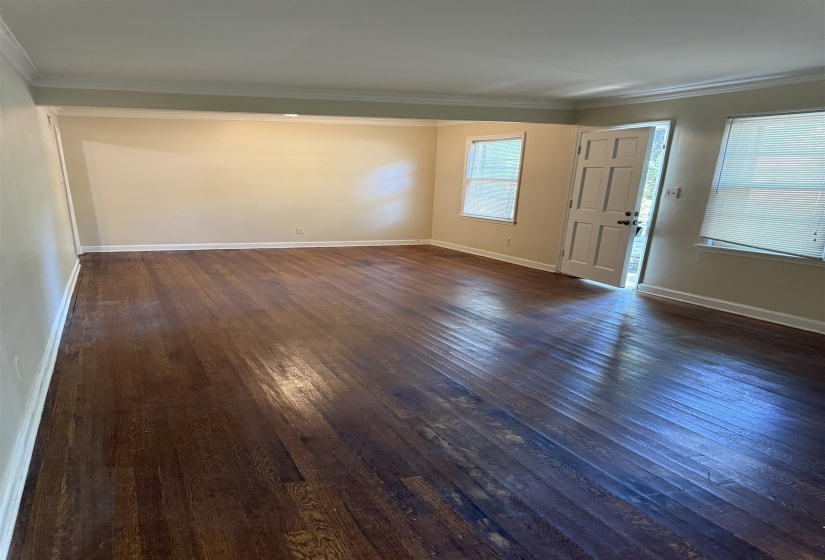 Spacious room featuring rich wood-finish flooring, neutral wall tones, white crown molding, and multiple windows with horizontal blinds