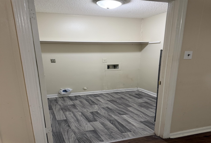 Dedicated utility area featuring wood-finish flooring and a built-in overhead shelf
