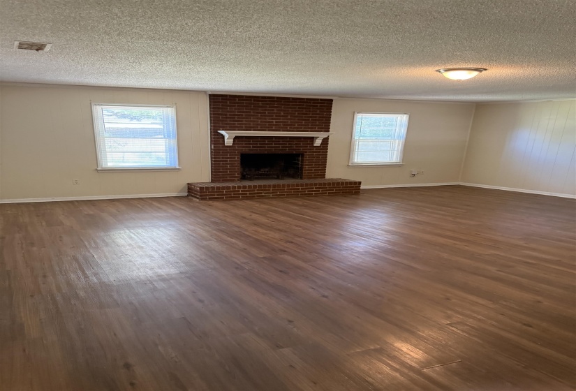 Spacious room featuring a brick fireplace with a white mantel, wood-finish flooring, and multiple windows
