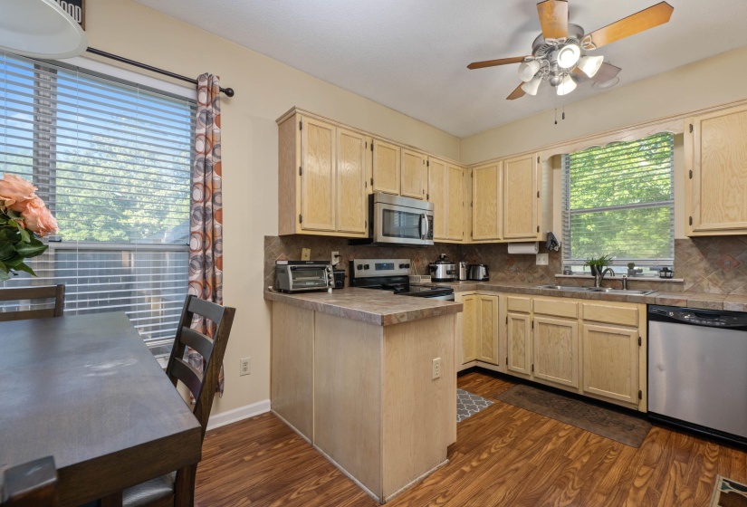 Eat-in kitchen featuring wood-finish flooring, light-toned cabinetry, stainless steel appliances, a tiled backsplash, and a ceiling fan