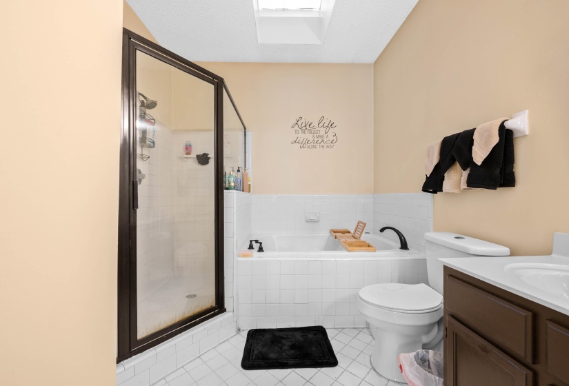 Bathroom featuring a glass-enclosed shower, built-in bathtub, white tiled flooring, a single vanity with dark cabinetry, and a skylight