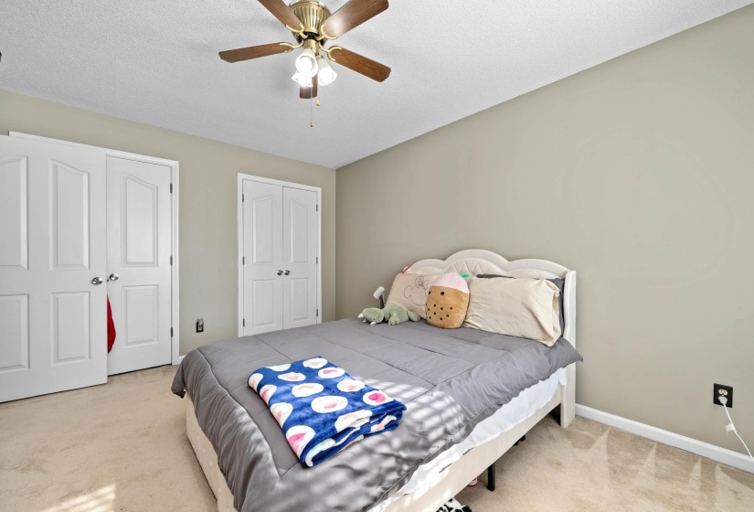 Bedroom featuring neutral wall paint, light-toned carpet, a ceiling fan with integrated lighting, and two sets of white bi-fold closet doors