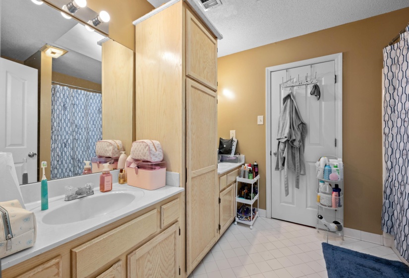 Bathroom featuring a light wood-finish vanity with an integrated sink, a large mirror, overhead vanity lighting, and a tall built-in storage cabinet