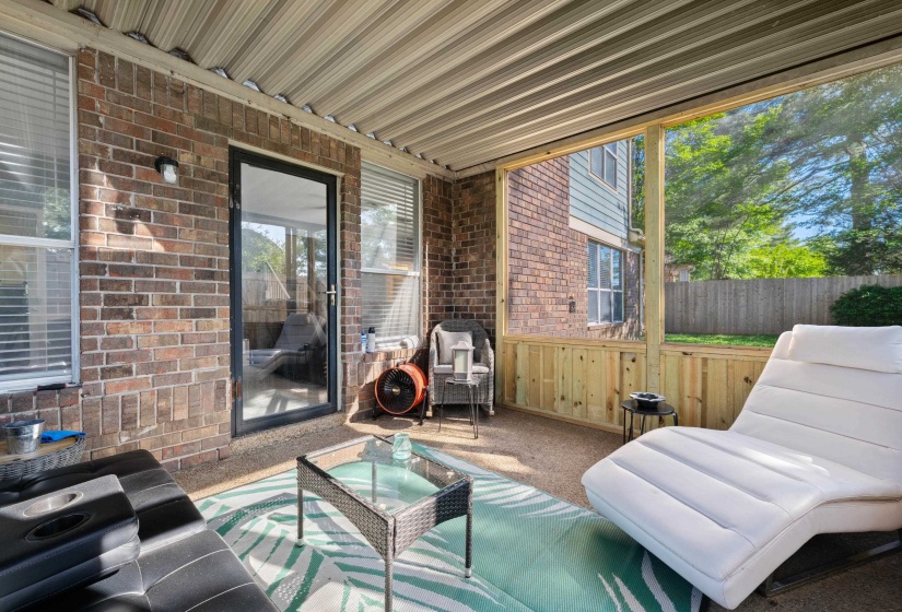 Screened patio featuring a corrugated metal roof, brick exterior wall, and a glass-paneled door
