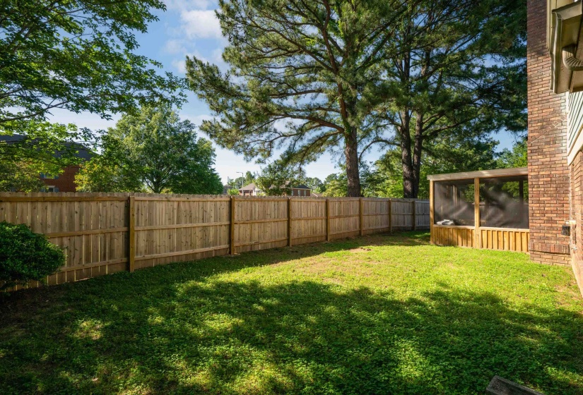 Expansive backyard with a full privacy fence, mature trees, and a screened-in structure