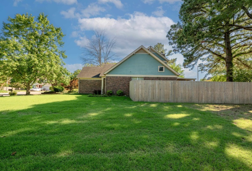 Expansive green lawn surrounds the property, featuring a wood privacy fence and mature trees
