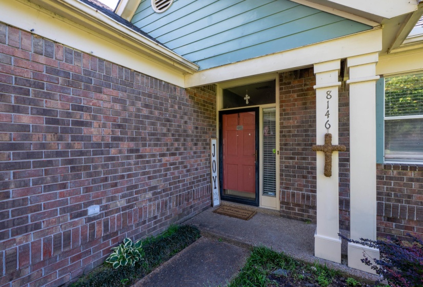 Brick exterior featuring a covered porch entry, red front door, and pale blue siding accents