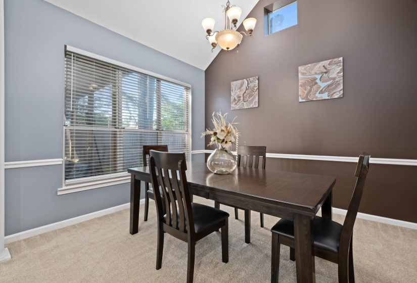 Dining area featuring vaulted ceilings, a prominent window with blinds, a built-in transom window, and a chandelier