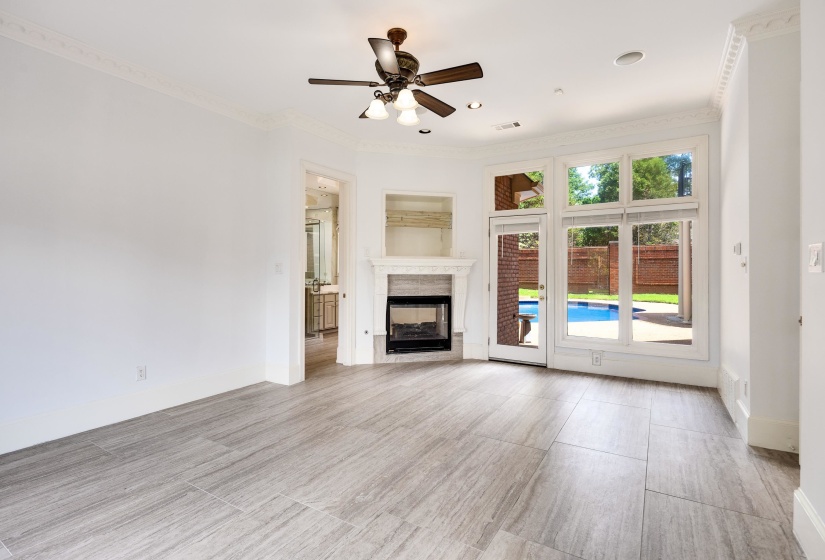 Spacious living area featuring large format tile flooring, a corner fireplace with a mantel, a ceiling fan, and extensive windows and a glass-paneled door opening to a private pool area