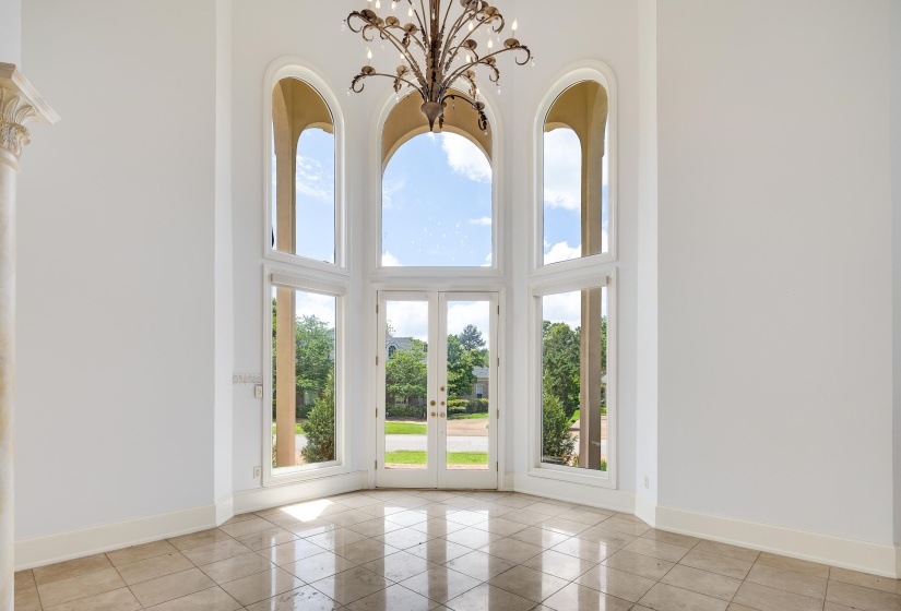 Grand entry featuring a tall arched window ensemble, French doors, a decorative chandelier, a fluted column with a Corinthian capital, and polished square tile flooring