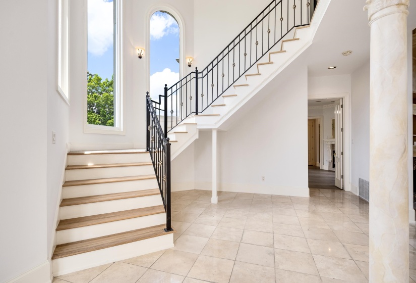 Grand staircase featuring wood-finish treads, white risers, and an ornate black wrought iron railing