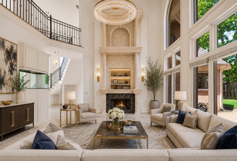 Great room featuring a two-story ceiling, a grand fireplace with stone mantel and marble surround, and expansive windows with arched transoms