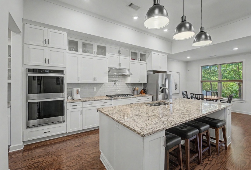 Open-concept kitchen featuring an expansive center island with a stone countertop, white cabinetry, integrated stainless steel appliances, and wood-finish flooring