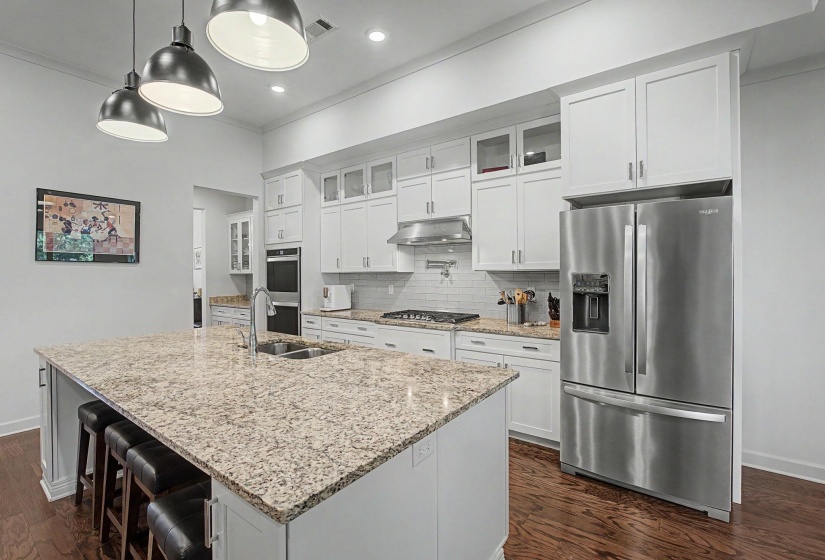 Kitchen featuring an oversized island with granite countertops, stainless steel appliances, white cabinetry, and wood-finish flooring