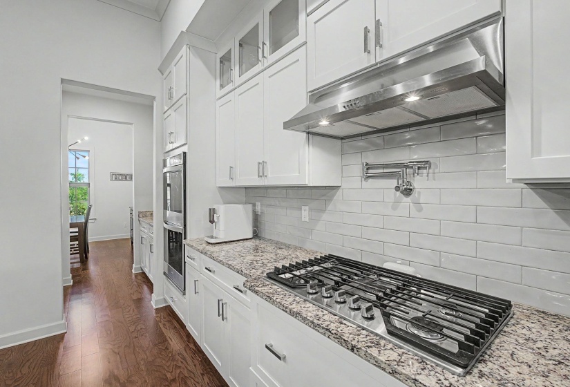 Kitchen featuring white cabinetry, a gas cooktop, stainless steel range hood, stone countertops, and a subway tile backsplash with a pot filler