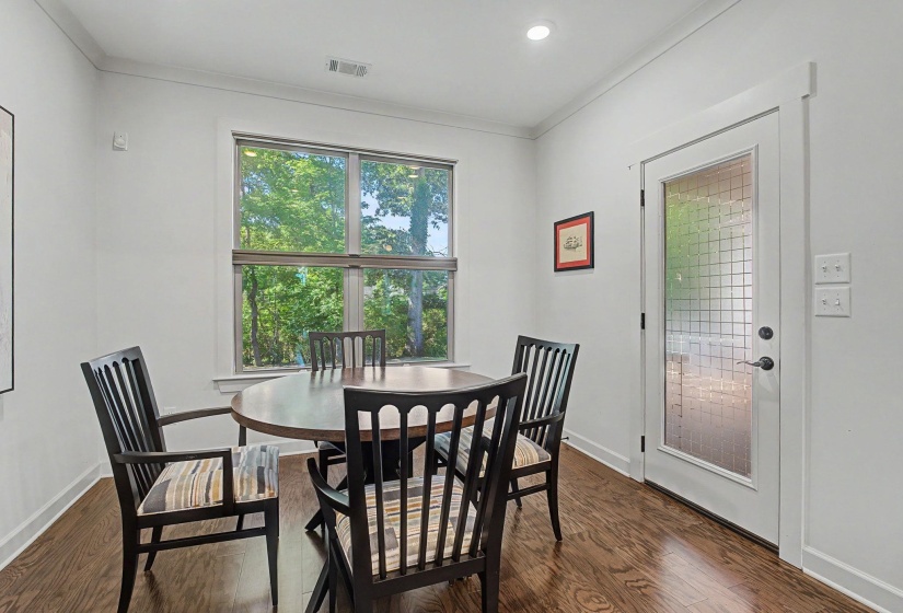 Bright interior space featuring a large window with exterior tree scenery, wood-finish flooring, recessed lighting, and a full-light door with decorative glass