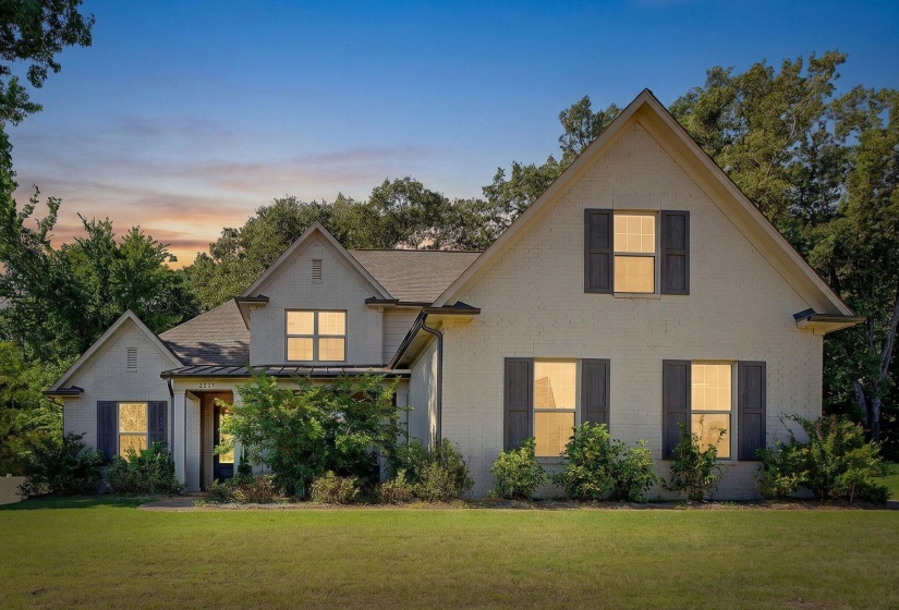 Traditional-style exterior featuring brick facade, gabled roofs, dark shutters, mature landscaping, and a manicured lawn