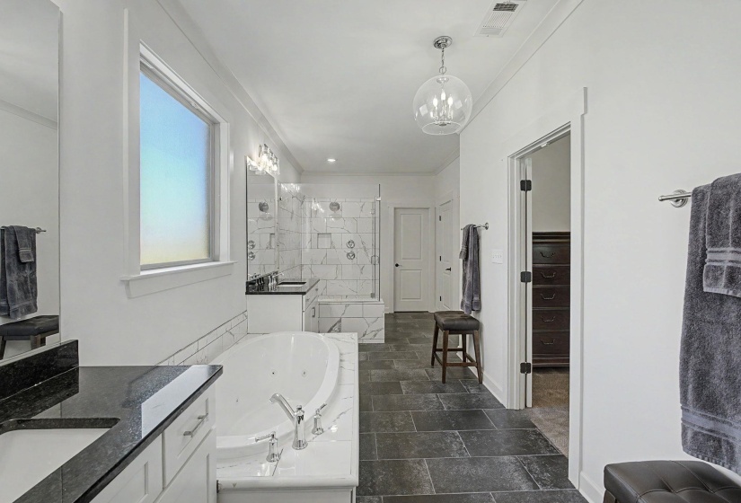 Spacious bathroom featuring a built-in jetted tub, dual vanity with dark countertops, white subway tile accents, a glass-enclosed shower, and large format dark tile flooring