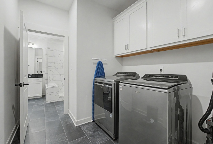 Laundry area featuring slate-look tile flooring, white shaker-style cabinetry with brushed nickel hardware, and a wood-finish shelf