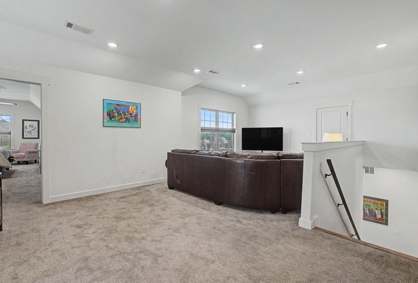 Carpeted loft area with recessed lighting, white walls, and a visible staircase with a black handrail